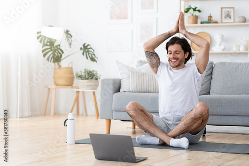 Happy guy practicing yoga in front of laptop