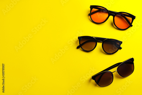 Many stylish sunglasses on yellow background, flat lay. Space for text