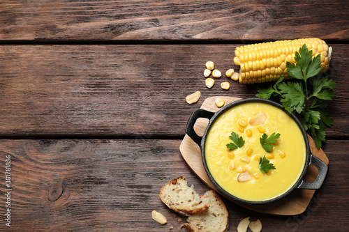 Delicious creamy corn soup, bread and cob on wooden table, flat lay. Space for text