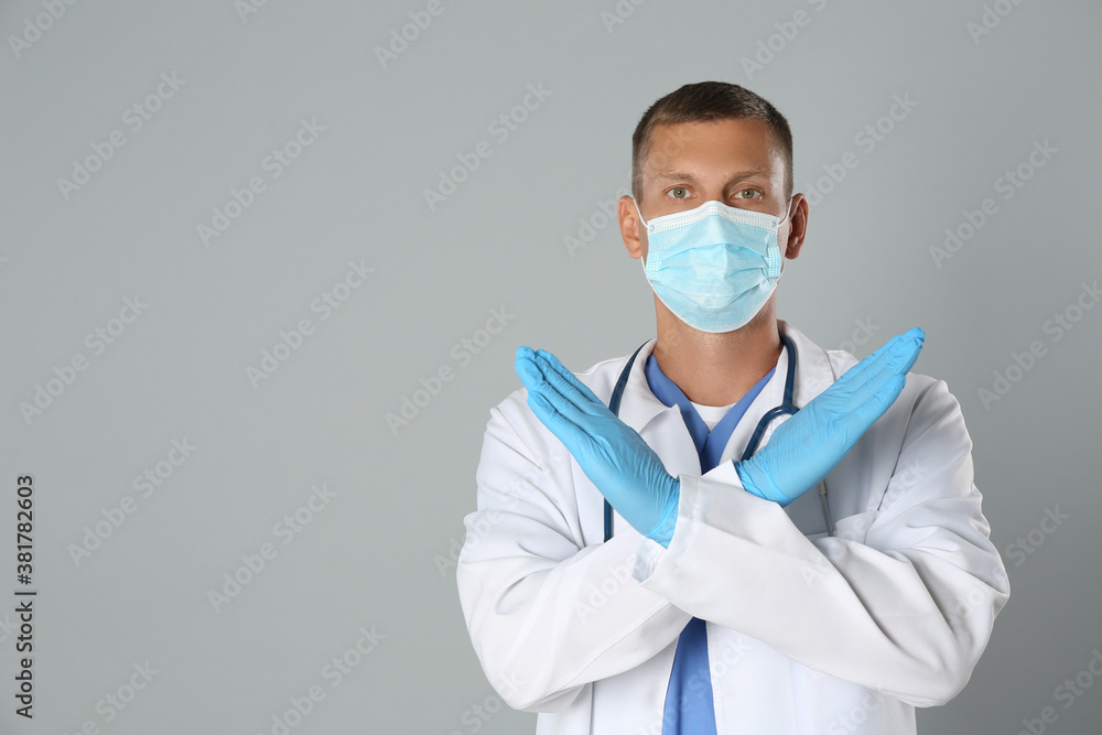 Doctor in protective mask showing stop gesture on grey background, space for text. Prevent spreading of coronavirus