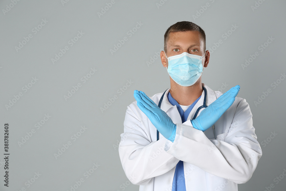 Doctor in protective mask showing stop gesture on grey background, space for text. Prevent spreading of coronavirus Doctor in protective mask showing stop gesture on grey background, space for text. Prevent spreading of coronavirus