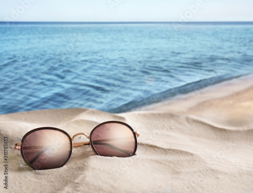 Stylish sunglasses on sandy beach near sea, space for text