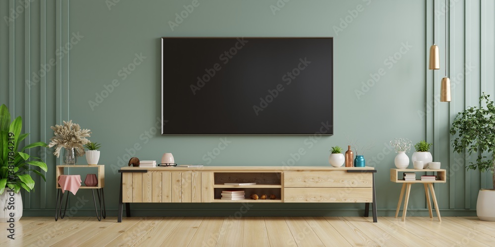 TV on cabinet in modern living room with armchair,lamp,table,flower and plant on dark green wall background.