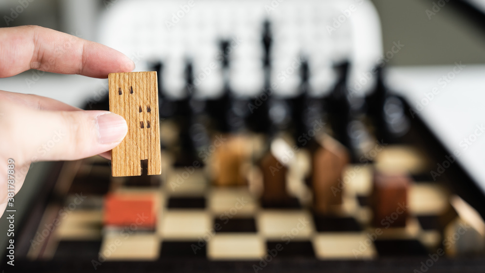 Hand of business man moving building and house models in chess game, competition success play. strategy, management or leadership concept Hand of business man moving building and house models in chess game, competition success play. strategy, management or leadership concept