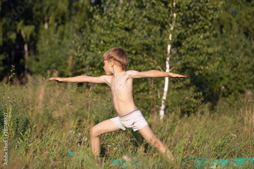 Young boy child practices yoga, standing of Yoga Warrior pose, exercising Virabhadrasana pose outdoor.