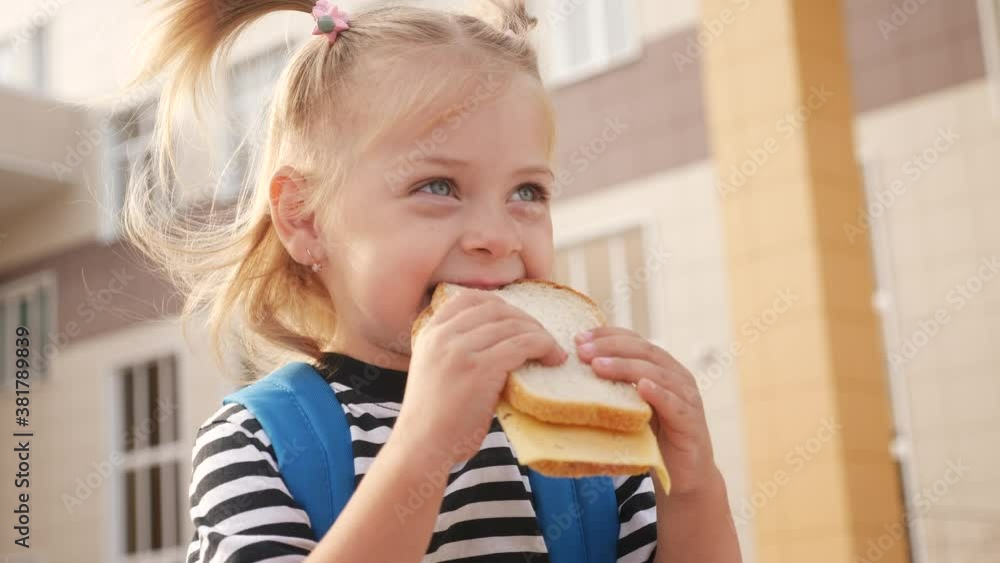 schoolgirl eating a sandwich during recess in school. kids education concept. little girl kid schoolgirl with a backpack eating a sandwich. kid child is having lunch at school lifestyle schoolgirl eating a sandwich during recess in school. kids education concept. little girl kid schoolgirl with a backpack eating a sandwich. kid child is having lunch at school lifestyle