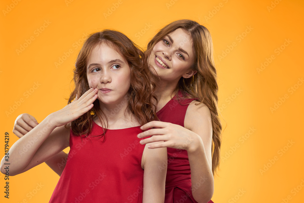 Happy woman and little girl in red dress are having fun on a yellow background fashion emotions sisters fun Copy Space. Happy woman and little girl in red dress are having fun on a yellow background fashion emotions sisters fun Copy Space.