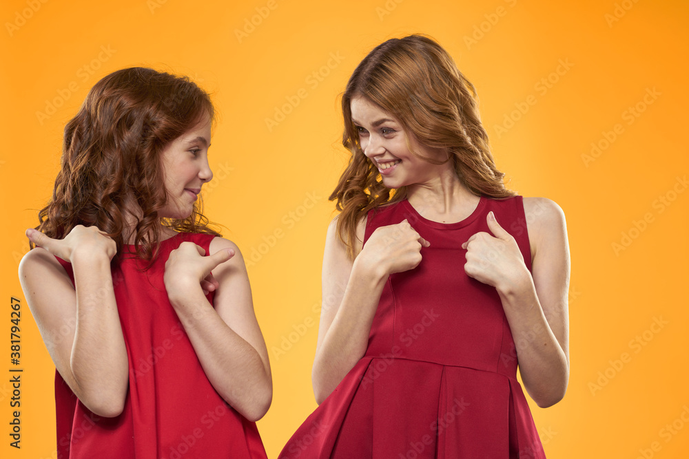 Happy woman and little girl in red dress are having fun on a yellow background fashion emotions sisters fun Copy Space. Happy woman and little girl in red dress are having fun on a yellow background fashion emotions sisters fun Copy Space.