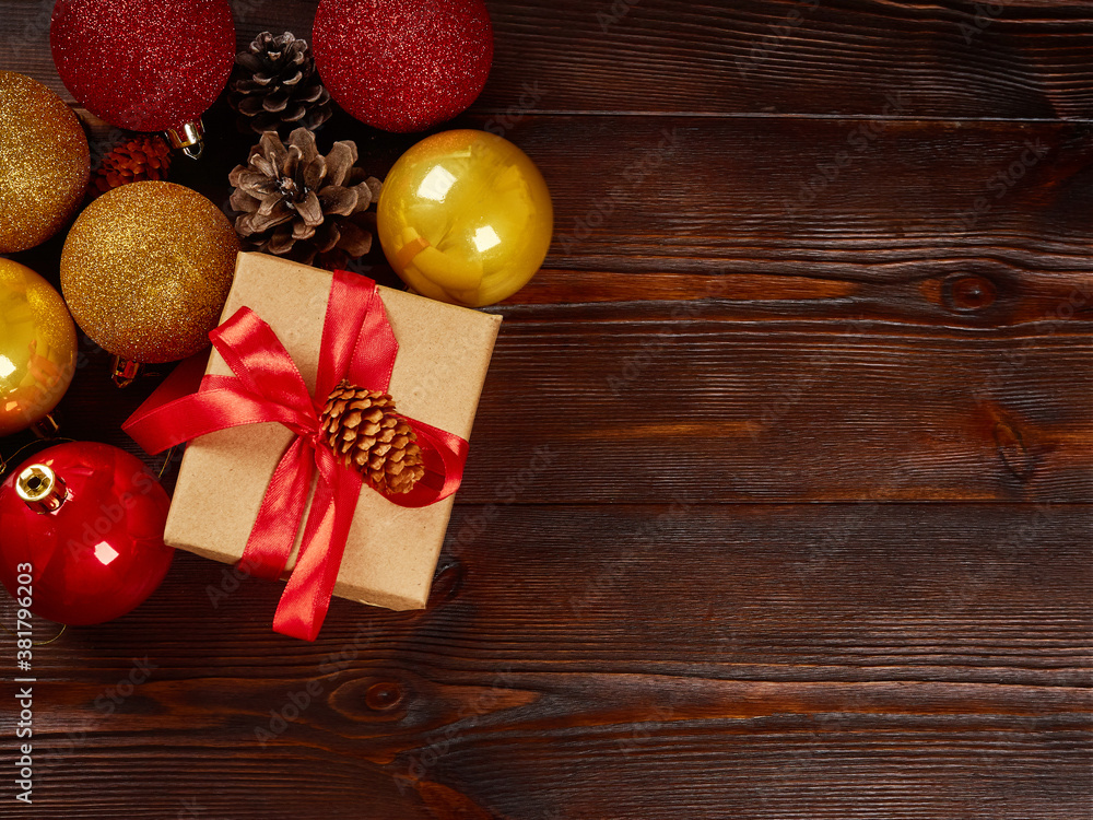 Christmas composition. Golden shiny balls, gift box with red ribbon, pine cones on a dark wooden background. Christmas composition. Golden shiny balls, gift box with red ribbon, pine cones on a dark wooden background.