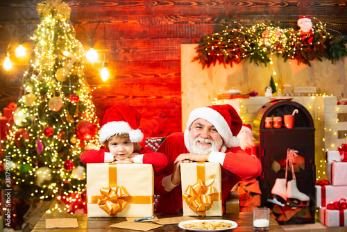 Christmas child. Surprised Little Santa in Christmas room. Santa Claus helper and grandfather with gifts. Believe in christmas miracle. photo