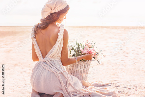 beautiful young stylish woman with basket with flowers outdoors at sunset