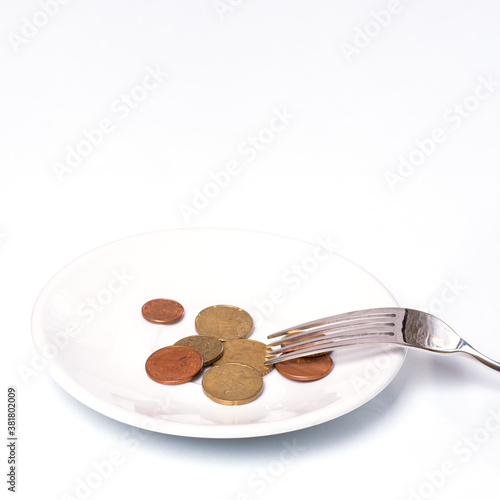 Euro cent coins on a white plate with a fork on a white background, close-up, copy space, vertical frame