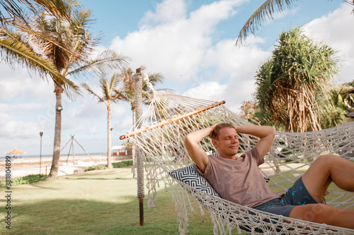Man relaxing in hammock on tropical beach with coconut palm trees, relaxation and leisure tourism, Bali island