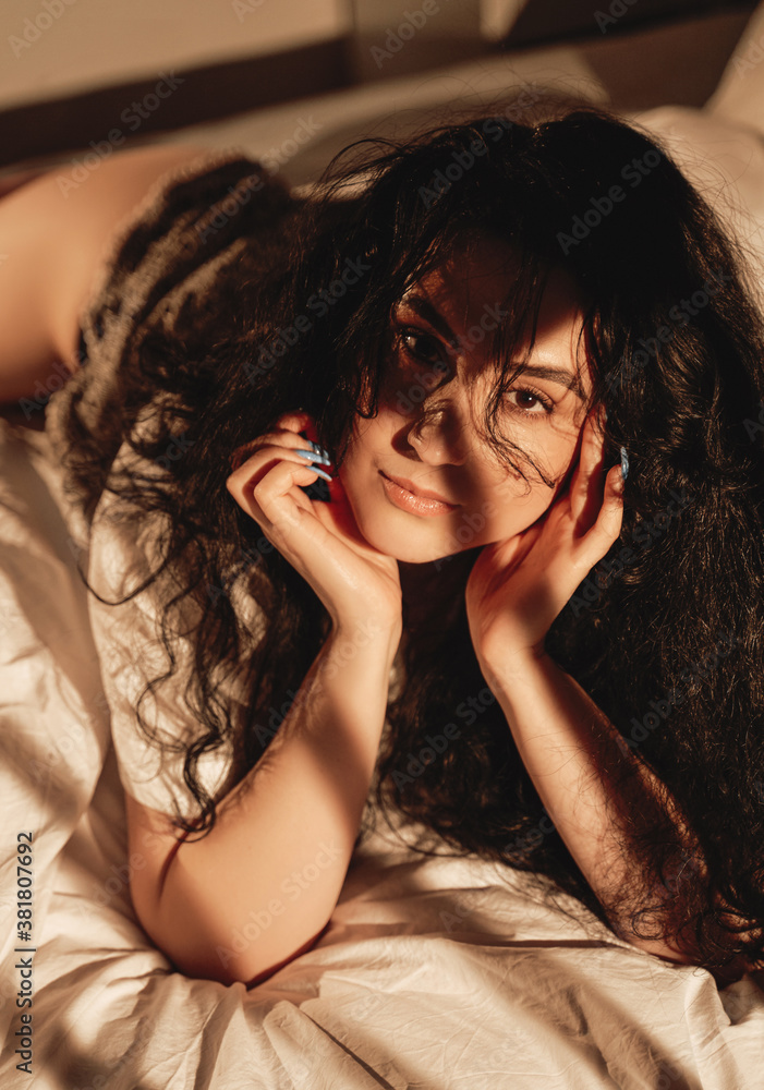 Cute brunette girl lying and resting on bed in warm apartment with contrast and fantasy shadows. Cute brunette girl lying and resting on bed in warm apartment with contrast and fantasy shadows.