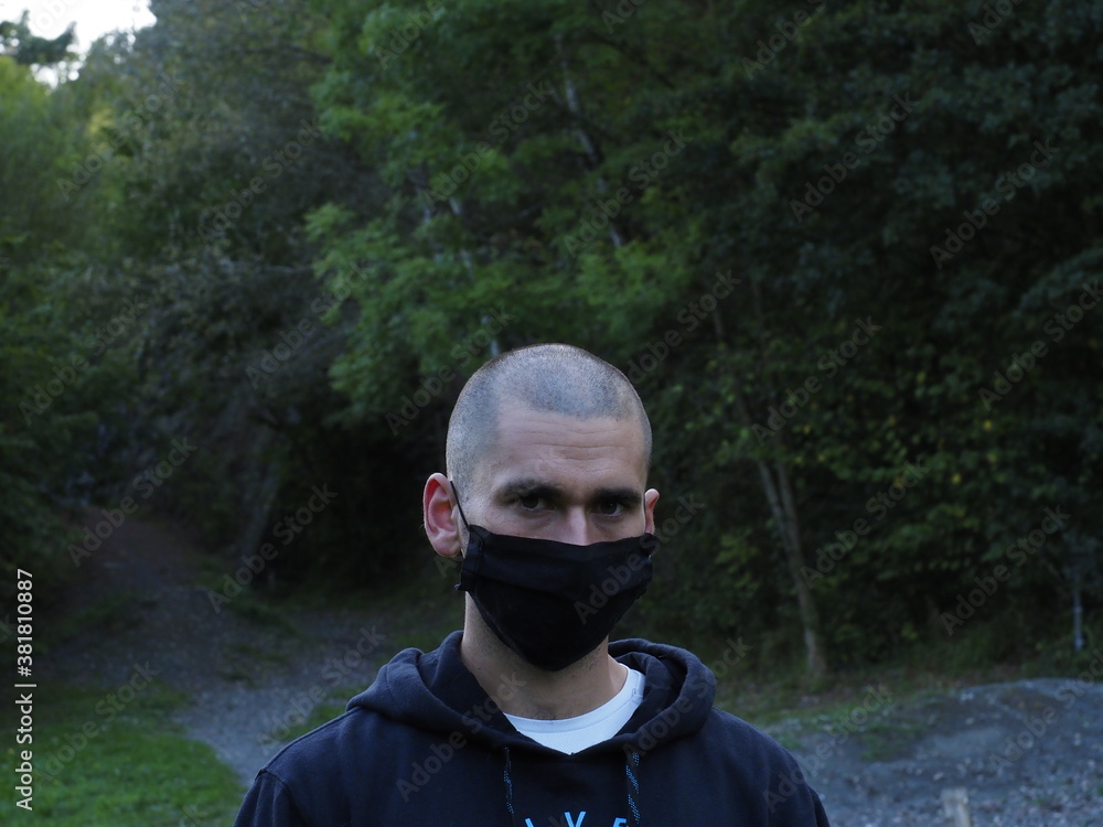 young man wearing a mask and a hood in a park young man wearing a mask and a hood in a park