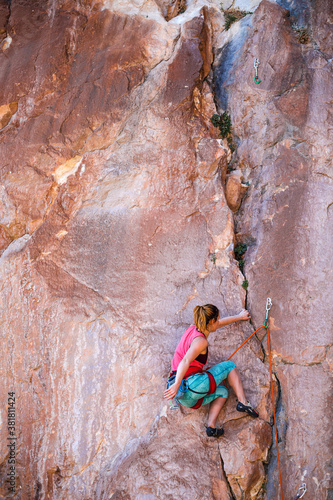 A strong woman climbs a beautiful orange rock.