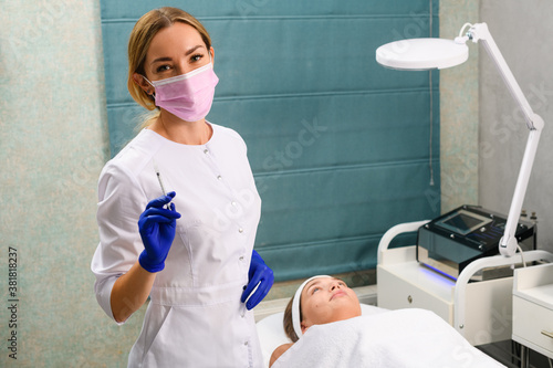 Happy cosmetologist with syringe and lying client