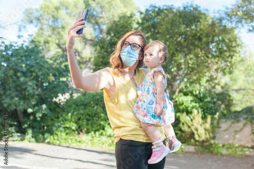 Mamá e hija tomándose un selfie con mascarilla en exteriores