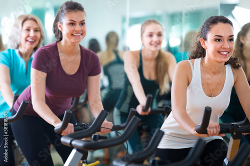 group of females riding stationary bicycles in modern gym for women