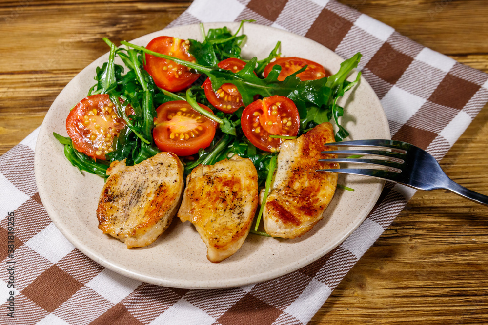 Fried chicken breast with salad of fresh arugula and cherry tomatoes on wooden table Fried chicken breast with salad of fresh arugula and cherry tomatoes on wooden table