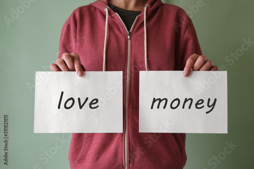 A young man holds a piece of paper with the words LOVE and MONEY.
