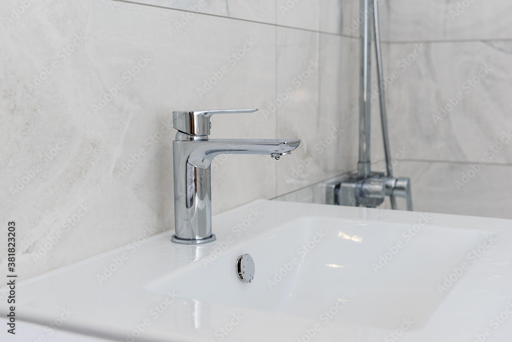 Faucet with a sink in the bathroom on a background of gray tiles. Faucet with a sink in the bathroom on a background of gray tiles.