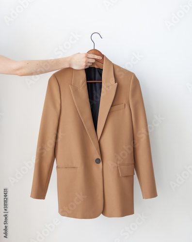 Konstfotografi A hand holds a classic beige jacket on a wooden hanger