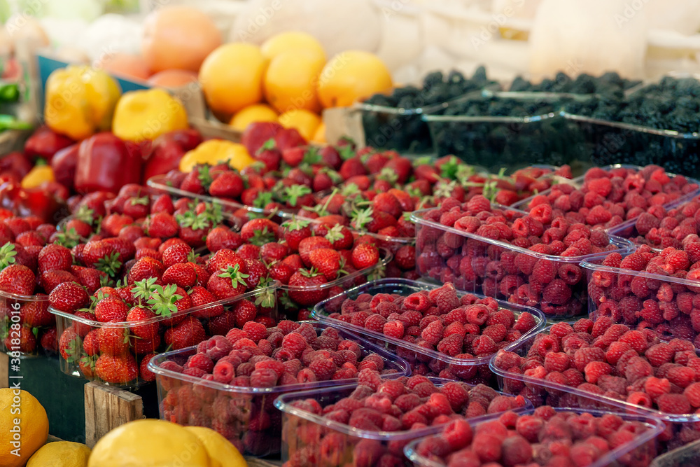 Blueberries, strawberries, raspberries and blackberries are prepared for sale at the farmers ' market. Fruits on the market counter are laid out in plastic containers. Fresh farm products