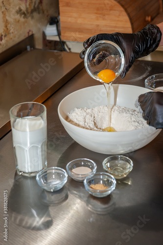 Baking a cake in a rural kitchen - a recipe for a dough made from the ingredients of eggs, flour, milk, yeast, sugar on a shiny table. The egg is added to the flour