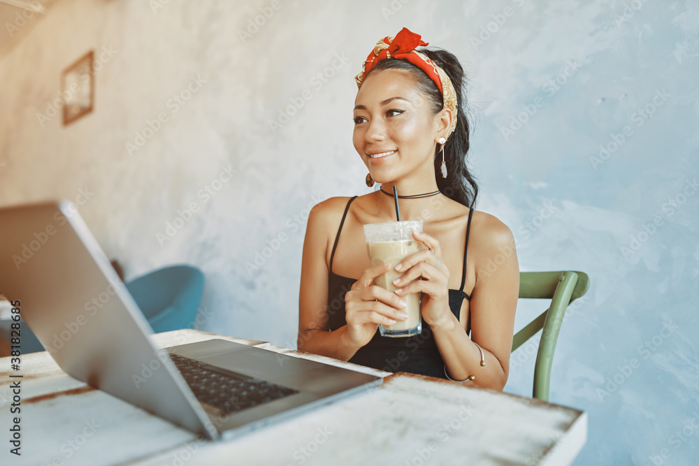 a young mixed race woman drink iced coffee and using her laptop in cafe
