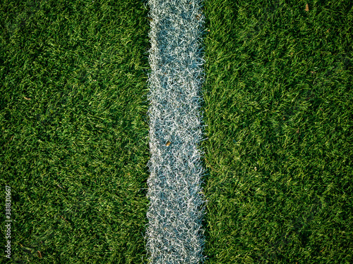 Close up image of white field lines of the penalty area on a football field with synthetic turf. White layout of the box line on a soccer field with green synthetic grass with warm autumn sun light.