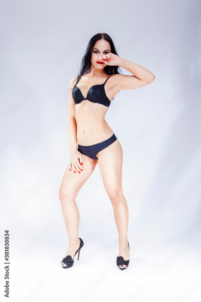 Full Length Portrait of Sensual Mature Caucasian Lady in Black Lingerie Posing Against White Background.