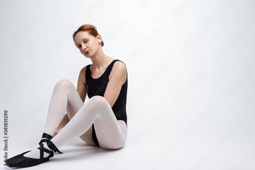 Portrait of Positive Caucasian Ballet Dancer in Body Suit and Pointes Shoes Against White Background.