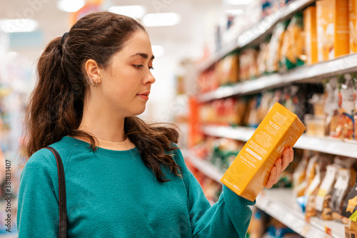 Portrait of a young Caucasian beautiful woman who reads the ingredients on the product packaging. Shelves with goods in a blur in the background. The concept of buying goods and shopping