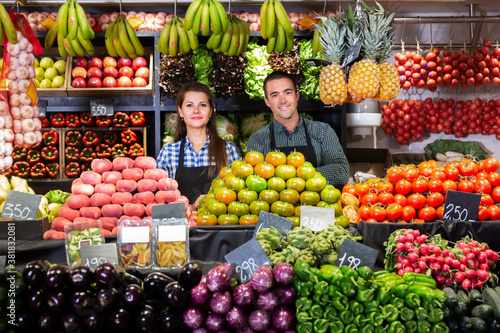 Portrait of young man and woman offering greens and vegetables in supermarket