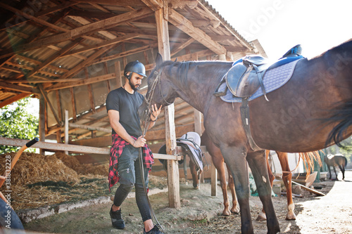 Arab tall beard man wear in black helmet with arabian horse.