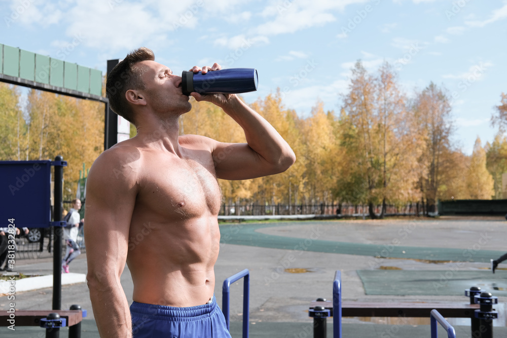 Obraz premium toned muscular man drinking whey protein cocktail after workout. autumn stadium, outdoors aclive training. shirtless man with a bottle of sport drink.