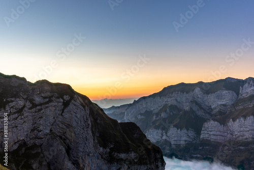 Colorful sunrise on the steep ridge of the majestic Schaefler peak in the Alpstein mountain range Appenzell, Switzerland with the fog covering the Seealpsee valley