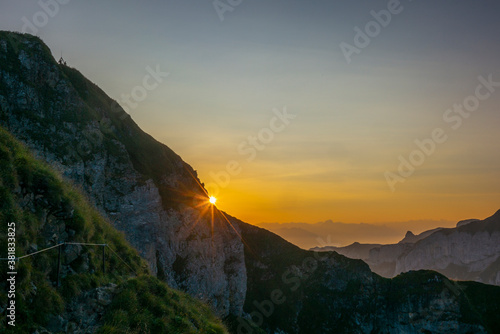 Hikers in the distance observing the colorful sunrise on the steep ridge of the majestic Schaefler peak in the Alpstein mountain range Appenzell, Switzerland photo