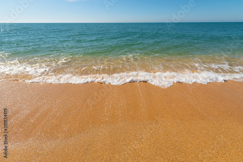 Morning turquoise sea and waves with white foam roll over the yellow golden sand of the beach. Ocean coast vacation concept