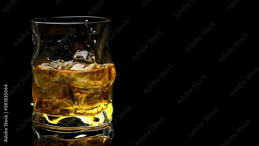 whiskey is poured into a crystal glass with ice on a black background whiskey is poured into a crystal glass with ice on a black background