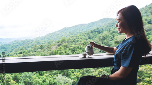 An asian woman pouring tea into a white cup on wooden table with beautiful mountain view