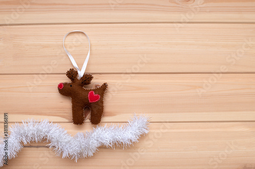 Christmas composition on a light wooden background. Brown Christmas deer made of felt stands on snow made of white tinsel .Flat bed, top view, copy space. Christmas frame, lyo's new year banner