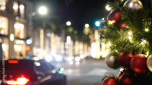 Closeup of Festively Decorated Outdoor Christmas tree with bright red balls on blurred sparkling fairy background. Defocused garland lights, Bokeh effect. Defocused night city street with cars on road