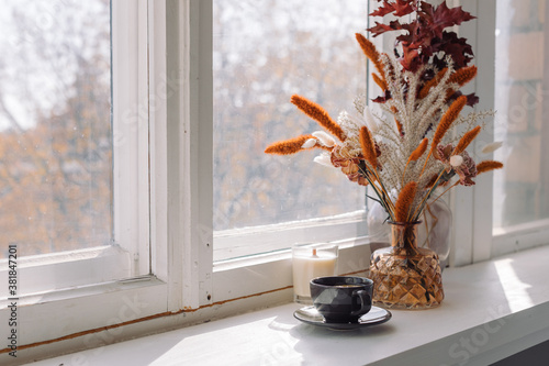 Cup of tea, flowers in vase on the window sill in morning light. Home decoration concept, fall colors, copy space. photo