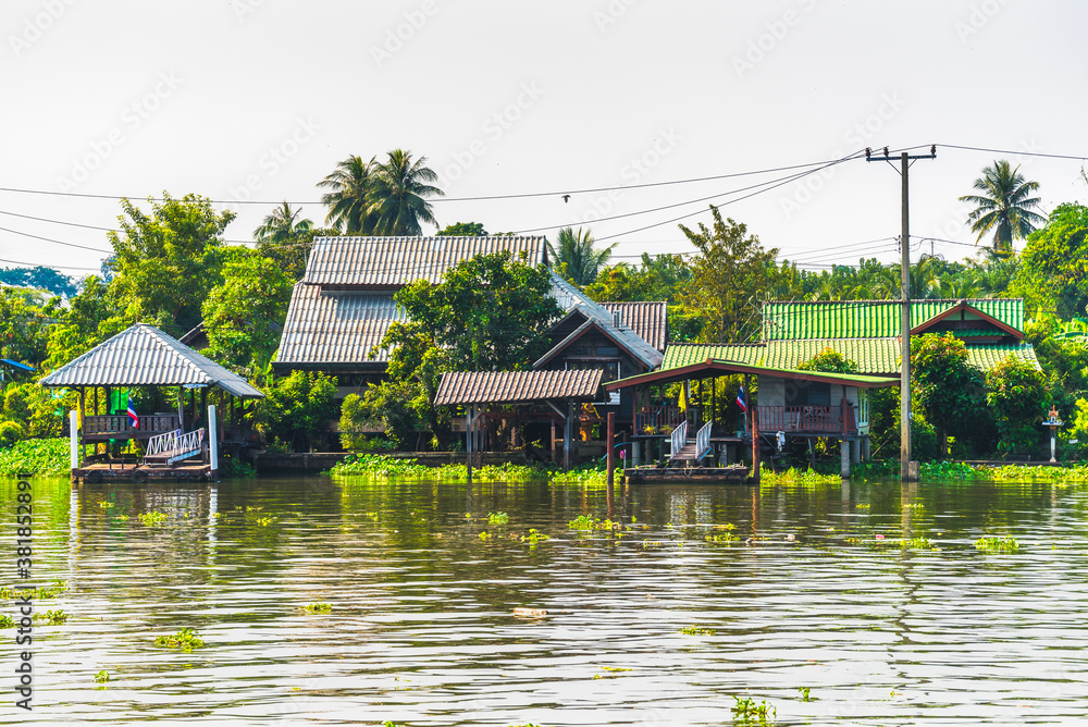 Obraz premium Stilt Houses at a Klong in Bangkok, Thailand. Chao Phraya Riverbank with Lush Vegetation.