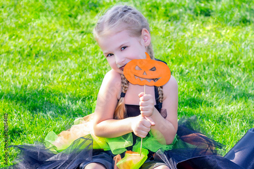 girl in a witch costume for the Halloween holiday. Happy girl sitting on the grass with pumpkins