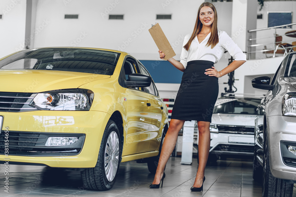 Attractive young female car dealer standing in showroom Attractive young female car dealer standing in showroom