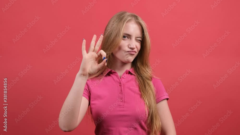 Close up of a happy young woman showing ok sign with fingers and winking isolated over a red background. Close up of a happy young woman showing ok sign with fingers and winking isolated over a red background.
