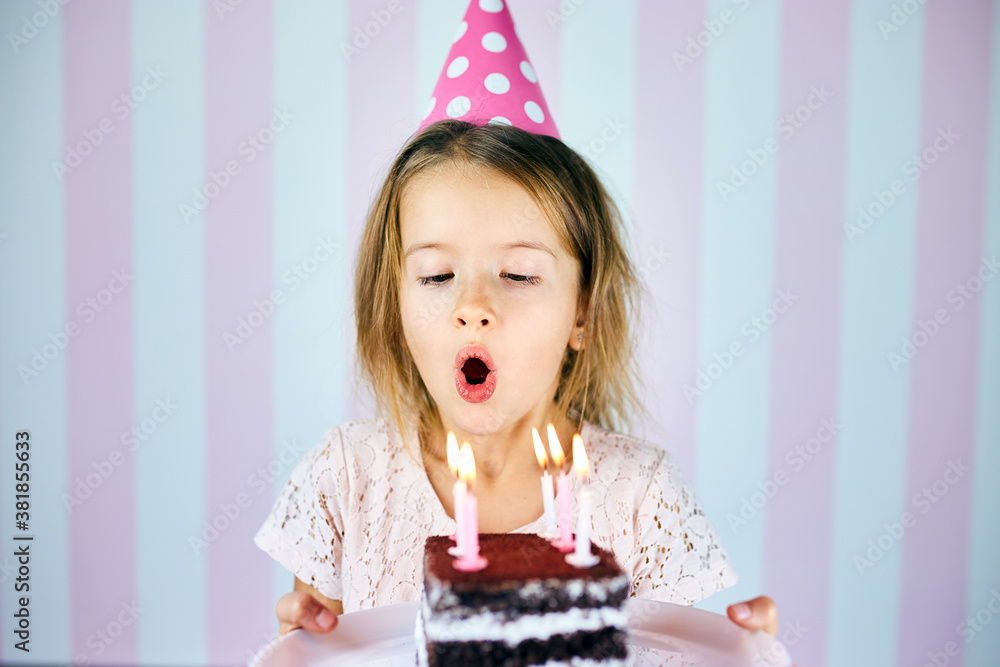 Little girl in pink cap blowing out candles on a birthday chocolate ...